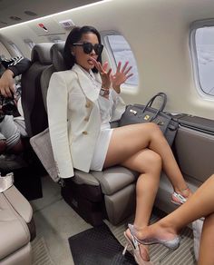 a woman sitting on an airplane with her legs crossed and one hand in the air