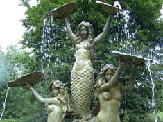 three mermaid statues holding trays in front of a fountain with water pouring from it