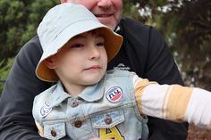 an older man holding a young boy in his arms and wearing a hat on top of him