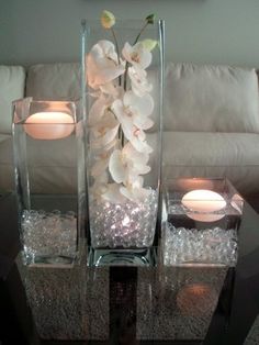 three glass vases with flowers and candles on a table in front of a couch