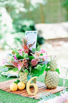 a pineapple centerpiece with flowers and fruit on a wooden table in the grass