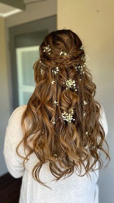 the back of a woman's head with long curly hair and flowers in her hair