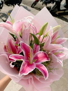 a bouquet of pink lilies is held by someone's hand on the sidewalk