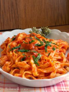 a white bowl filled with pasta and sauce on top of a checkered table cloth