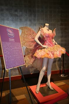 a statue of a woman dressed as a fairy holding an umbrella and standing next to a sign