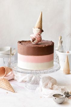 a cake with ice cream and chocolate frosting on a glass platter next to cones