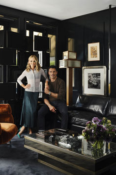 a man and woman sitting on a couch in a living room with black walls behind them