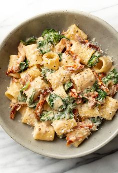 a bowl filled with pasta and spinach on top of a marble countertop next to a fork