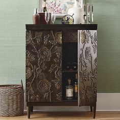 an ornate cabinet with wine glasses and bottles on it in front of a green wall