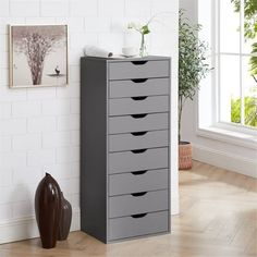 a tall gray cabinet with five drawers next to a window