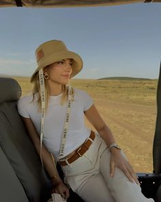 a woman sitting in the back seat of a vehicle wearing a hat and white pants