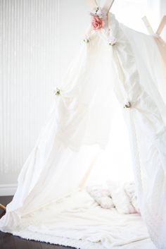 a white teepee with flowers hanging from it's sides on the floor in front of a window