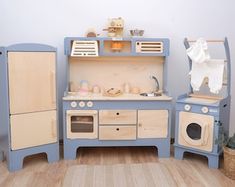 a wooden toy kitchen with blue cabinets and white appliances