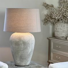 a table lamp sitting on top of a dresser next to a vase filled with flowers