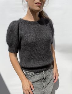 a woman standing in front of a white wall with her hands on her hips and looking at the camera