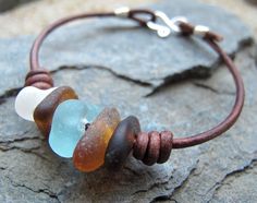 a leather bracelet with sea glass beads and silver clasps on a stone slab surface