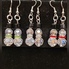 four pairs of earrings with swarong and crystal beads hanging from hooks on a black surface