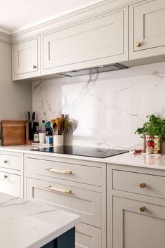 a kitchen with white cabinets and marble counter tops, gold pulls on the cabinet doors