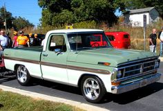 an old pick up truck is parked on the side of the road with people standing around