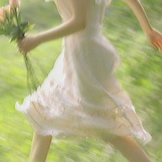 a woman in a white dress is holding a bouquet of flowers and running through the grass