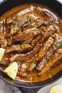 steaks and sauce in a skillet with lemon wedges on the side for garnish