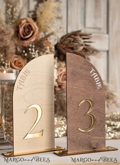 two wooden table numbers with candles and flowers in the background on a white table cloth