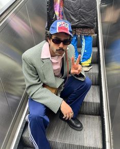 a man sitting on an escalator giving the peace sign with his hand while wearing sunglasses and a hat