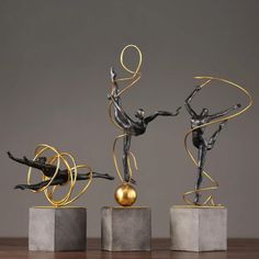 three metal sculptures on pedestals with one holding an apple and the other standing up