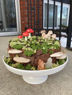 a cake with moss and mushrooms on it sitting in front of a brick building,