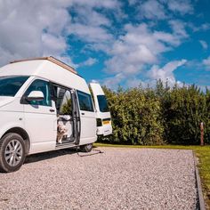 a white van is parked on gravel with its door open and a dog in the driver's seat