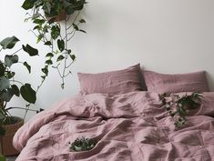 an unmade bed with pink sheets and plants