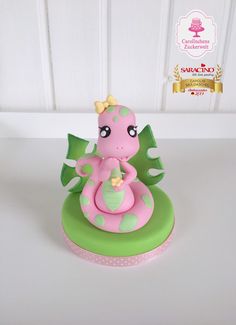 a pink and green cake with a little dragon on it's head sitting on top of a table