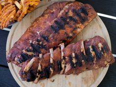 two pieces of meat on a wooden plate next to french fries