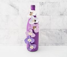 a purple bottle with flowers on it sitting in front of a marble wall and floor