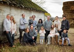 a group of people standing next to each other in front of a wooden building with hay bales