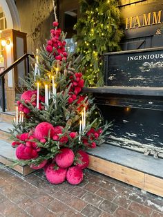 a small christmas tree with red balls and candles on the front steps in front of a store