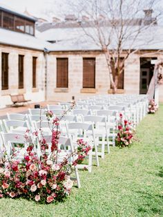 rows of white chairs with pink flowers on them in front of an old brick building