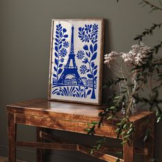 a blue and white painting sitting on top of a wooden table next to a vase with flowers