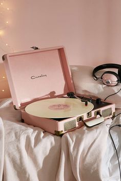 a record player sitting on top of a bed next to headphones and a pink suitcase