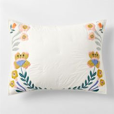 an embroidered pillow with flowers and leaves on the front, sitting on a white surface