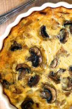 a mushroom and cheese quiche on a wooden table with a serving utensil