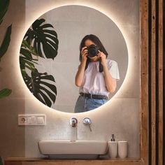 a woman taking a photo in front of a bathroom mirror with a plant behind her