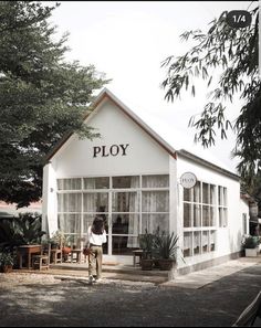 a person standing in front of a white building with plants on the outside and windows that say ploy