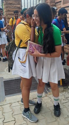 two girls are hugging each other in front of a building with people standing around them