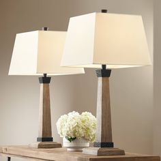 two lamps sitting on top of a wooden table next to a vase with white flowers