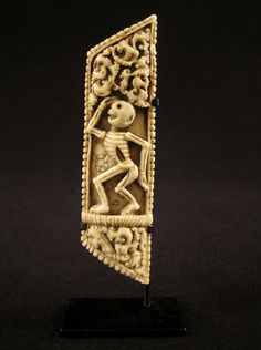 a carved ivory figurine depicting a skeleton carrying a human body on a black background