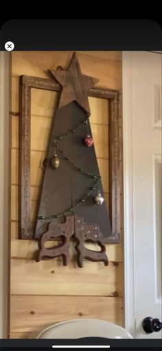 a christmas tree is hanging on the wall in front of a wooden frame with an ornament