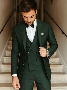 a man wearing a green suit and bow tie standing in front of stairs with his hand on his hip