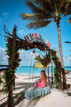 a woman is sitting on a swing at the beach