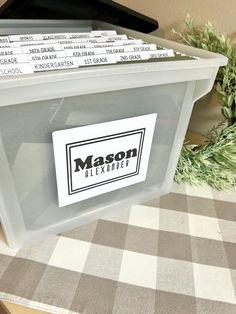 a plastic container with labels on it sitting on a checkered table cloth next to a potted plant